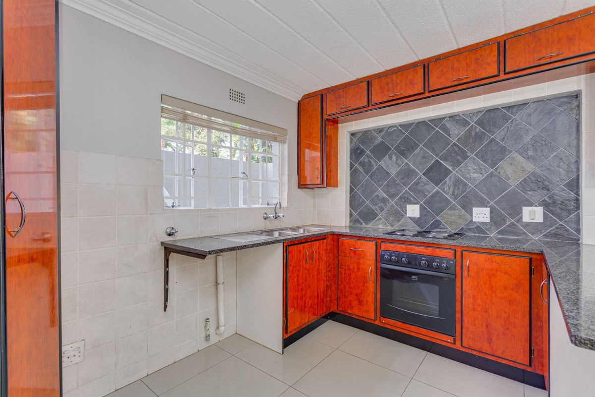 A functional kitchen featuring wood-finish cabinetry, granite countertops, built-in oven, electric hob, and tiled splashbacks with ample natural light.
