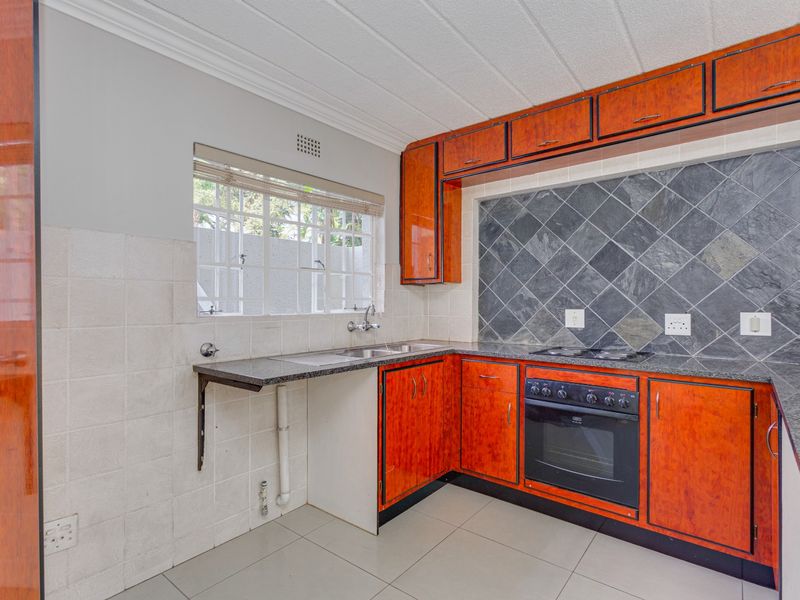 A functional kitchen featuring wood-finish cabinetry, granite countertops, built-in oven, electric hob, and tiled splashbacks with ample natural light.