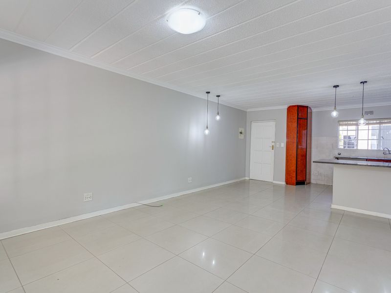 Spacious open-plan living and kitchen area featuring neutral tiled flooring, modern pendant lighting, and a functional breakfast bar layout.