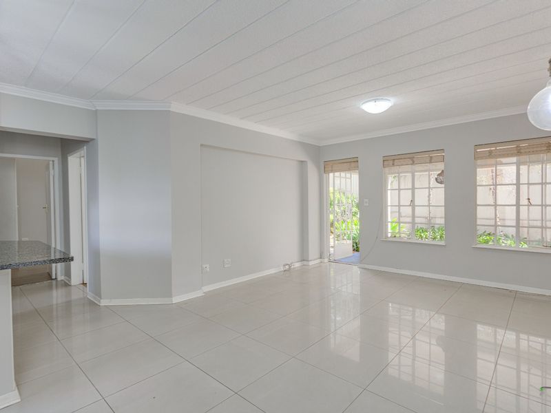 Spacious open-plan living area featuring neutral tiled flooring, modern granite kitchen counter, and large windows providing natural light and garden access.