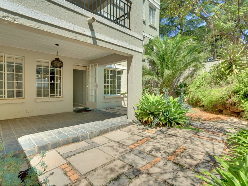 A ground floor apartment featuring a covered tiled patio, paved garden area, and direct access through french doors.
