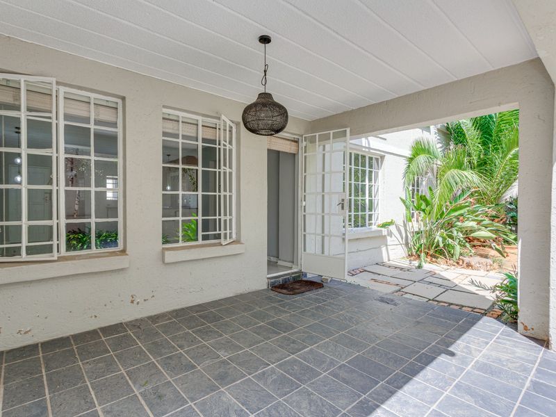 A covered patio area featuring tiled flooring, steel-framed windows, and direct access to a small garden space.