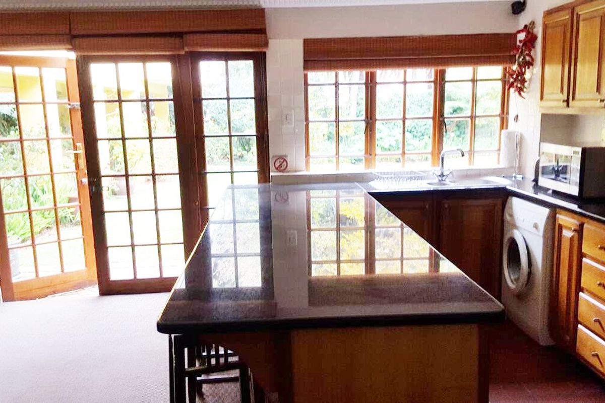 A functional kitchen featuring wooden cabinetry, granite countertops, and direct access to the garden through large french doors.
