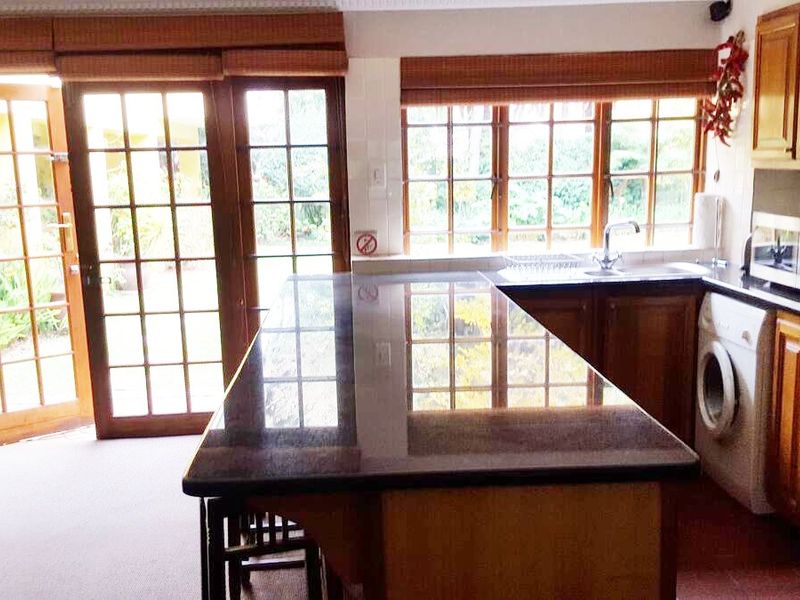 A functional kitchen featuring wooden cabinetry, granite countertops, and direct access to the garden through large french doors.