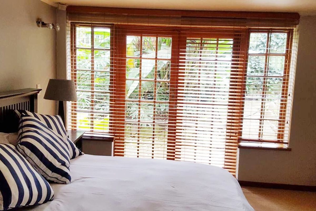 A bedroom featuring wooden-framed windows and french doors with venetian blinds, providing natural light and garden views.