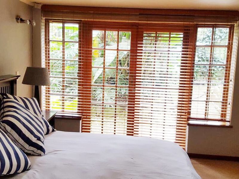 A bedroom featuring wooden-framed windows and french doors with venetian blinds, providing natural light and garden views.