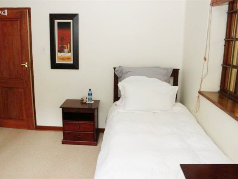 A compact bedroom featuring neutral walls, carpeted flooring, and a timber door and window frame.