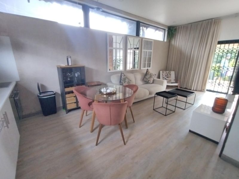 An open-plan living and dining area featuring light-toned laminate flooring, clerestory windows for natural light, and direct access to an outdoor space via a security gate.