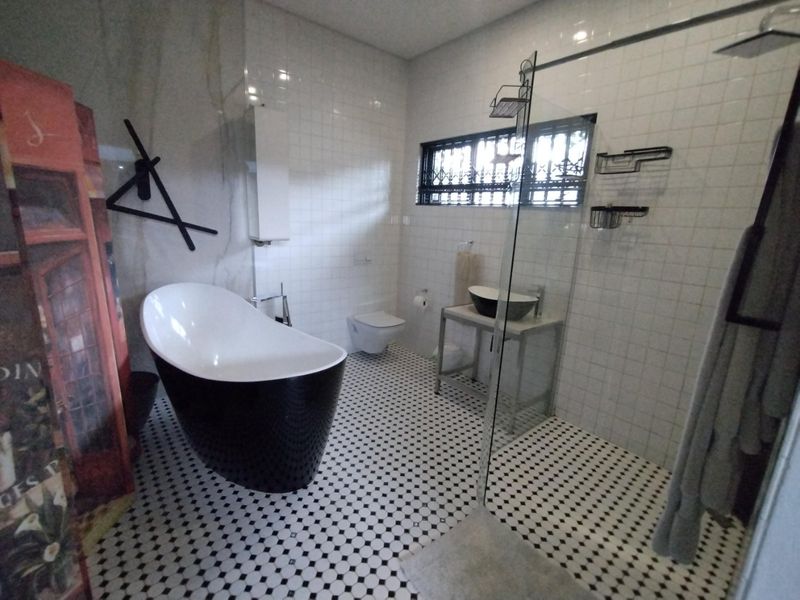 Modern bathroom featuring a sleek freestanding bathtub, a spacious walk-in shower with glass screen, wall-mounted toilet, and stylish monochrome tiled flooring.