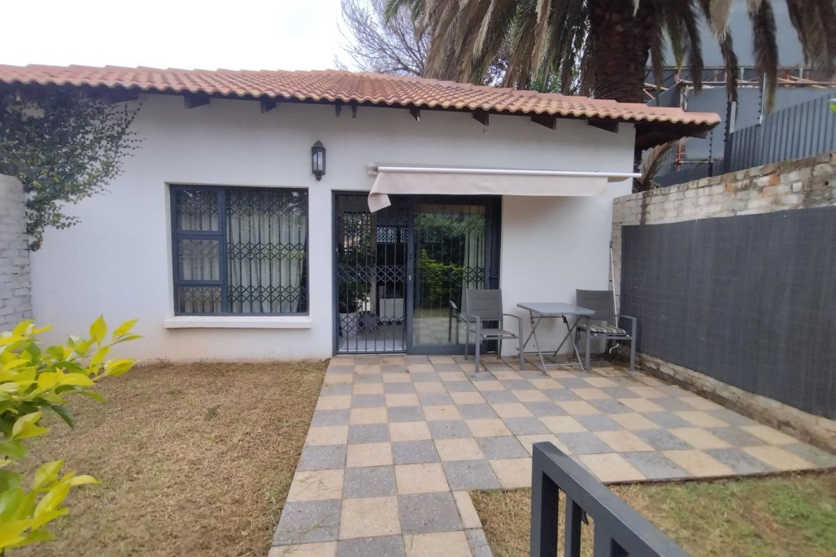 Rear exterior view of the townhouse featuring a paved patio area, retractable awning, and direct access through a sliding door with security gate.