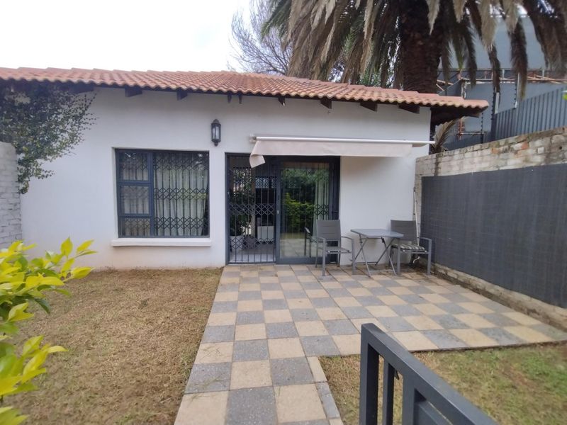 Rear exterior view of the townhouse featuring a paved patio area, retractable awning, and direct access through a sliding door with security gate.