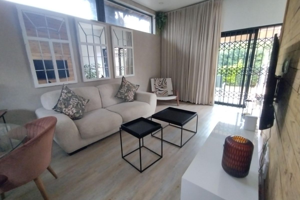A bright living room featuring light-toned laminate flooring, clerestory windows for natural light, and a sliding glass door with security gate access to the exterior.