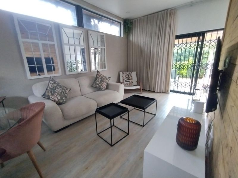 A bright living room featuring light-toned laminate flooring, clerestory windows for natural light, and a sliding glass door with security gate access to the exterior.