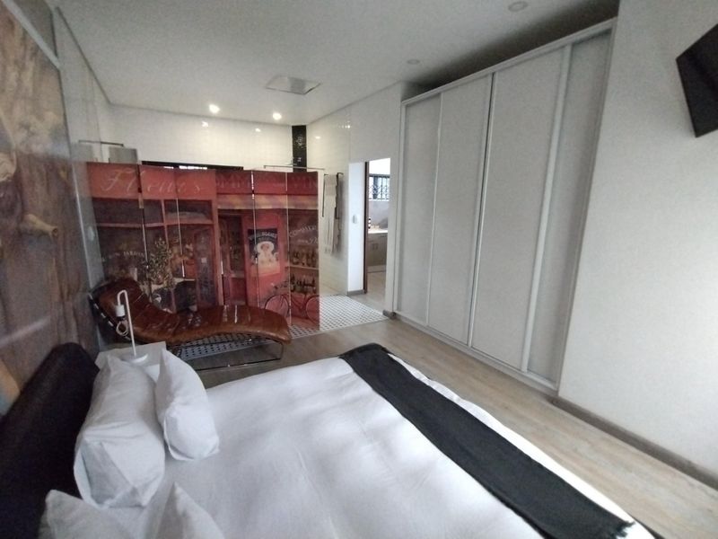 Spacious bedroom featuring modern laminate flooring, built-in wardrobes, and recessed lighting, with an open-plan layout leading to an en-suite bathroom area.