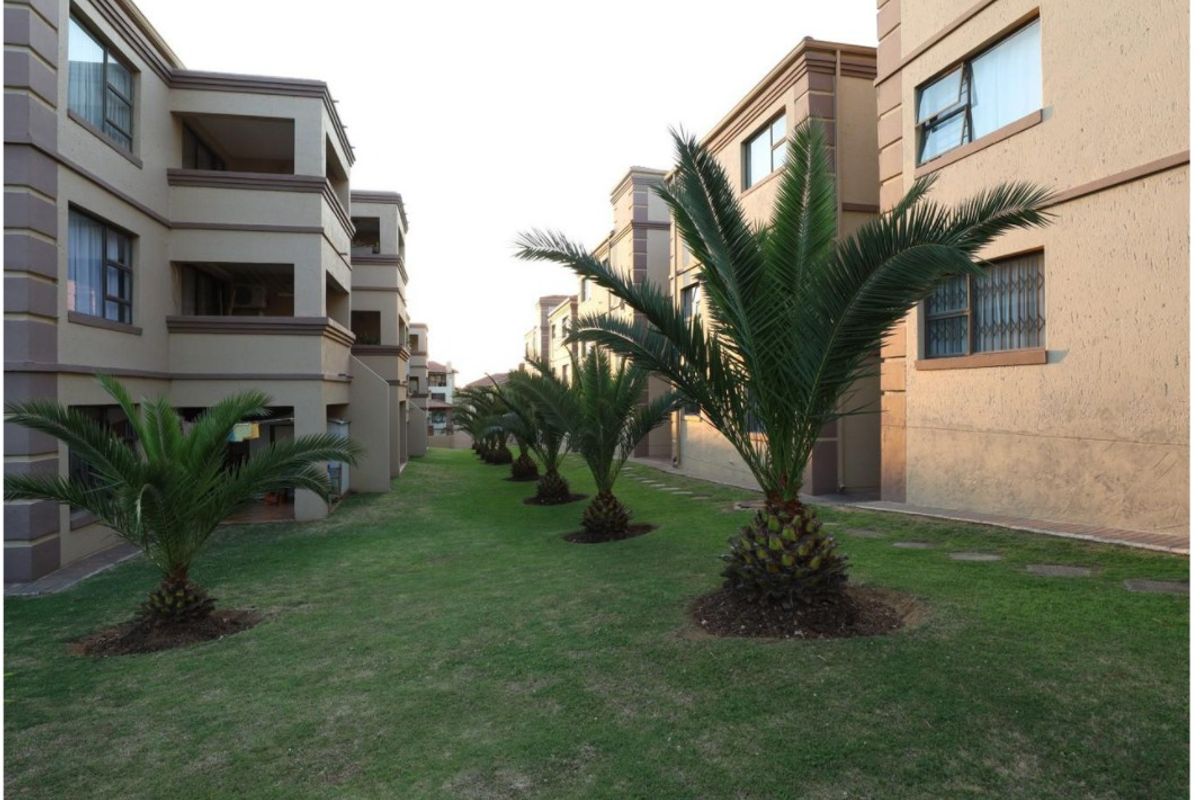 A view of the communal garden area between townhouse blocks, featuring well-maintained lawns and established palm trees.