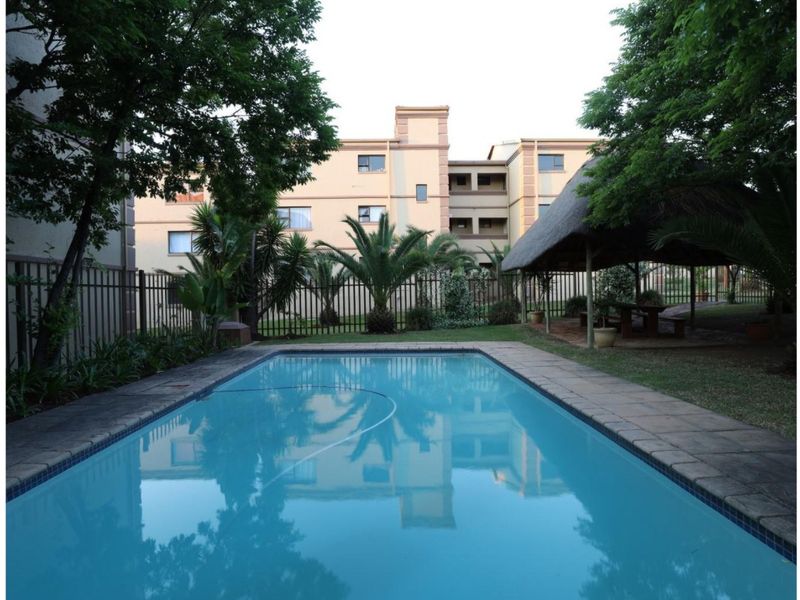 Communal swimming pool area featuring a thatch lapa, paved surround, and established garden within a secure townhouse complex.
