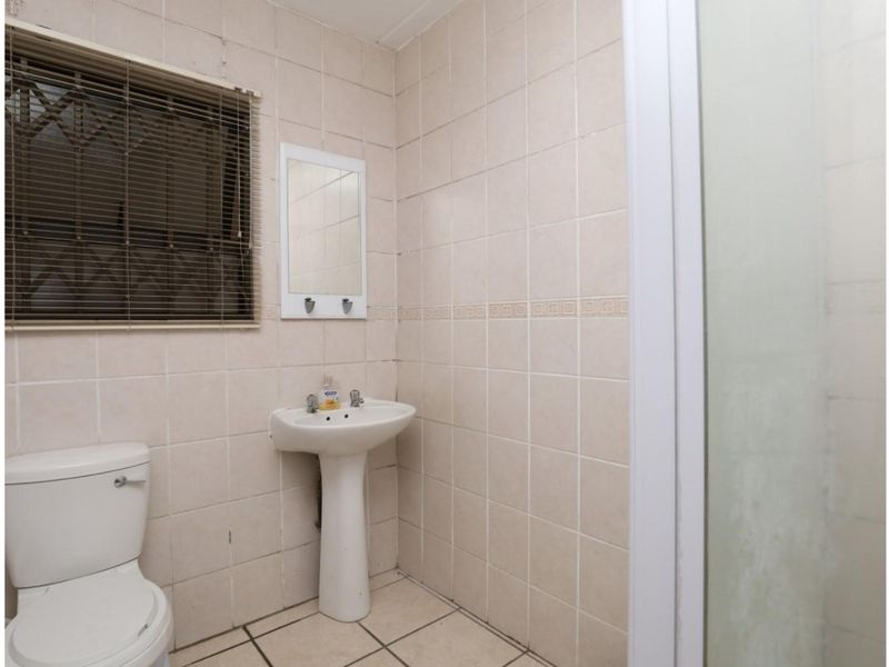A functional bathroom featuring a pedestal basin, toilet, and shower enclosure with full-height wall tiling and tiled flooring.
