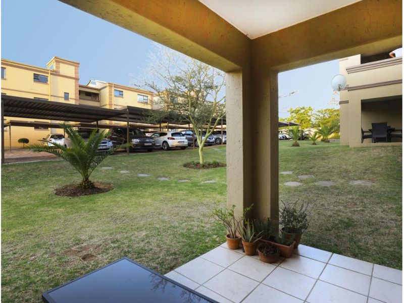 A covered patio area with tiled flooring overlooking a communal garden and parking area within the townhouse complex.
