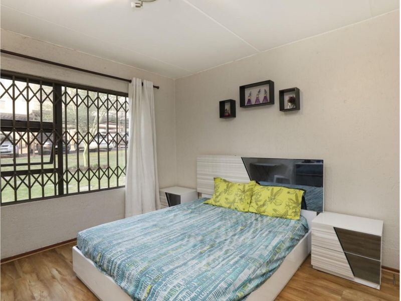 A bedroom featuring laminate flooring and a window fitted with a metal security gate, providing a functional and secure living space.