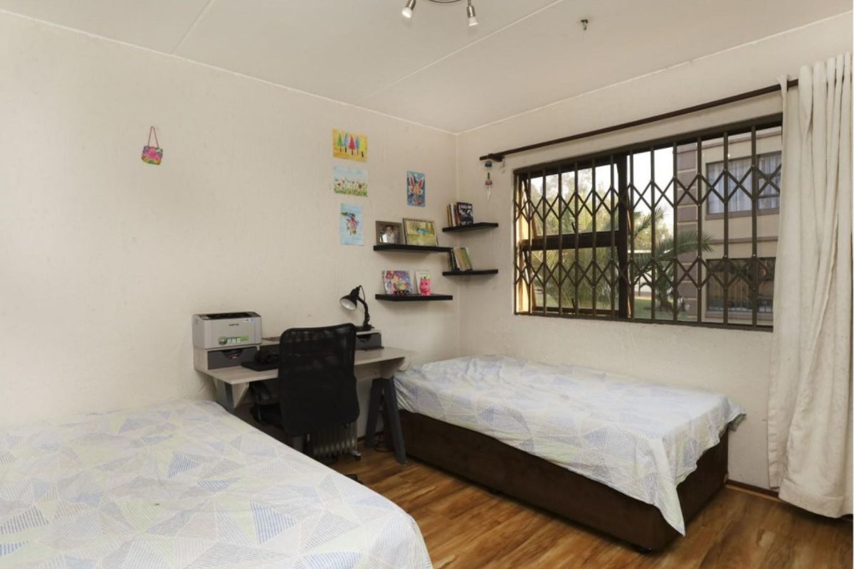A functional bedroom featuring laminate flooring, a window with a security gate, and a central ceiling light fixture.