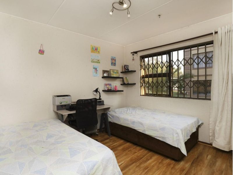 A functional bedroom featuring laminate flooring, a window with a security gate, and a central ceiling light fixture.
