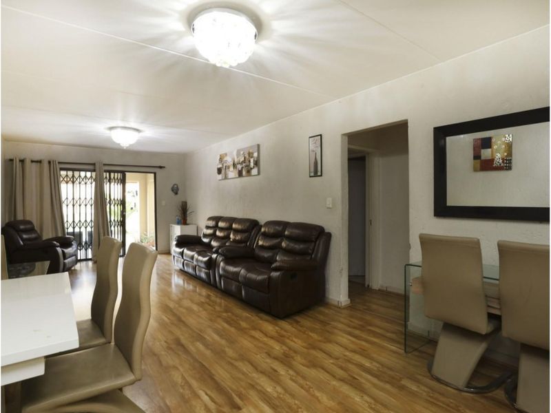 Spacious open-plan living and dining area featuring laminate flooring, neutral walls, and sliding glass doors leading to an outdoor space.