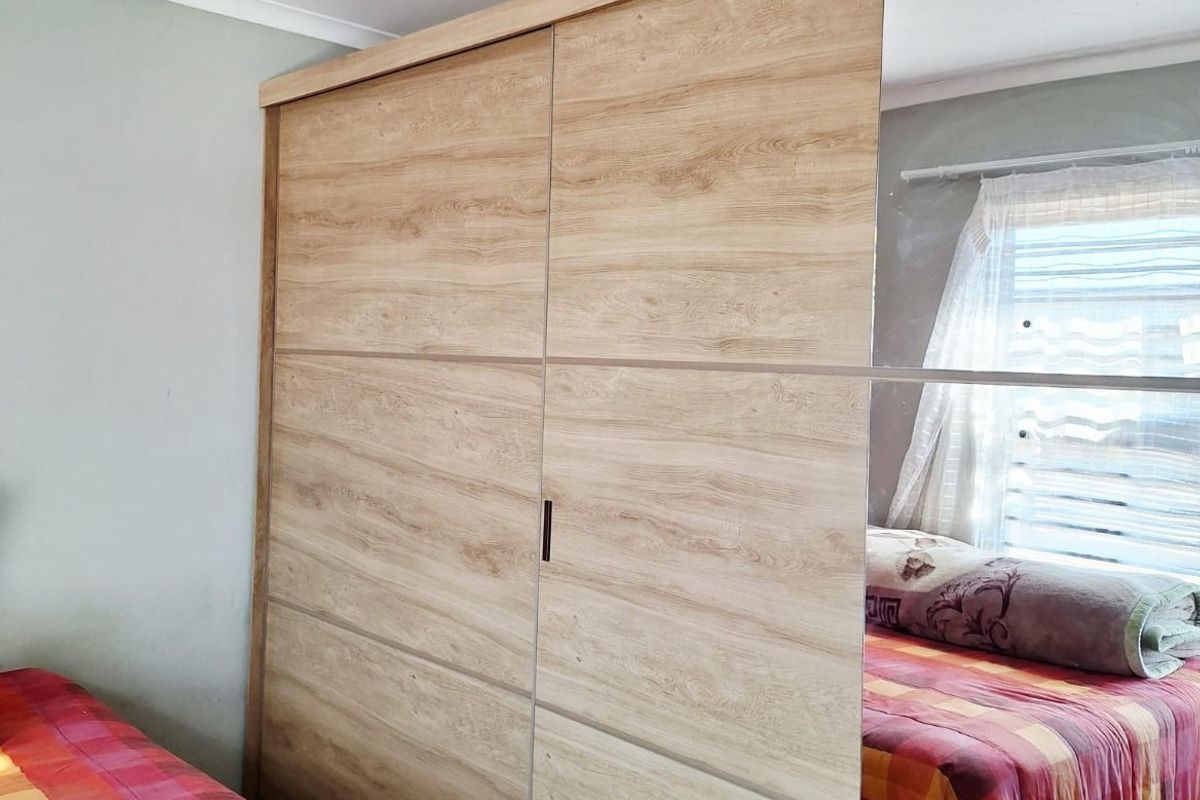 A bedroom featuring a large, modern built-in wardrobe with wood-grain finish and mirrored sliding doors.