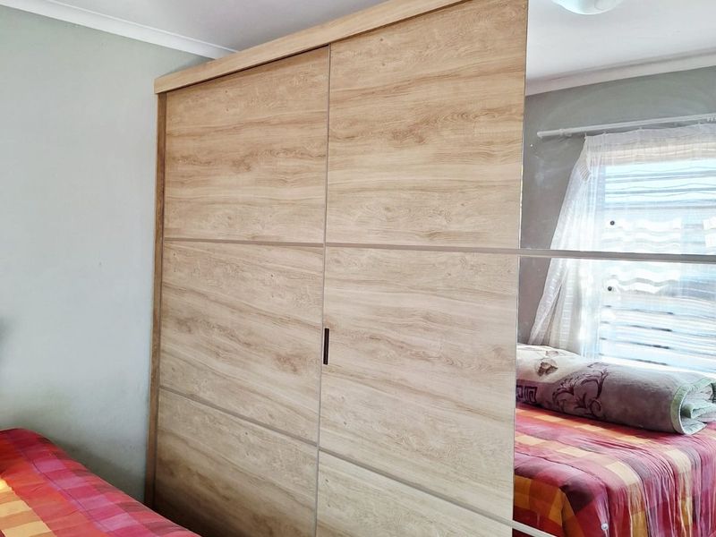 A bedroom featuring a large, modern built-in wardrobe with wood-grain finish and mirrored sliding doors.