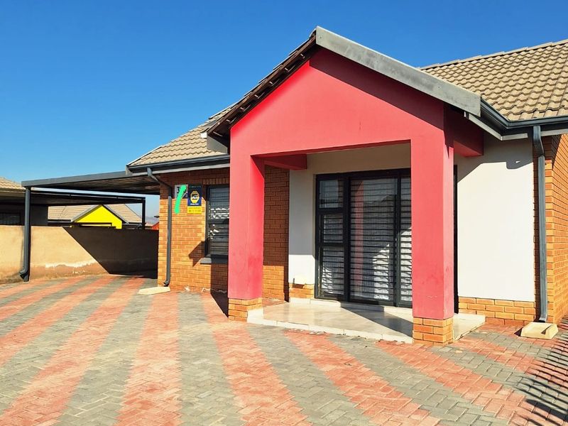 Front elevation of a residential house featuring a brick facade, tiled roof, paved driveway, and an attached carport.