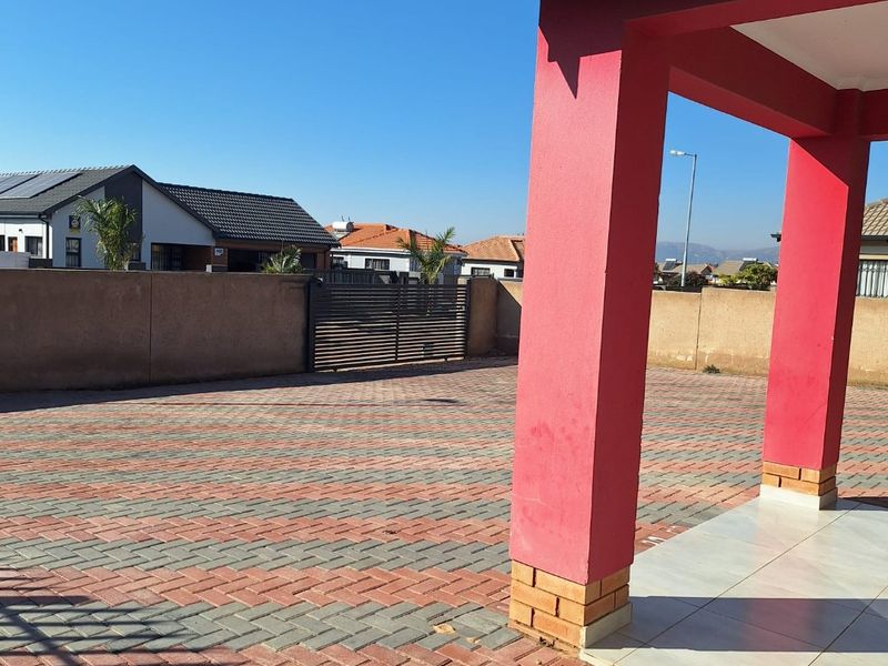 A paved front driveway and entrance area featuring a covered porch with tiled flooring and a secure boundary wall with a metal gate.
