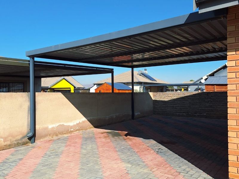 A functional outdoor carport featuring a metal roof structure and paved driveway, enclosed by boundary walls.