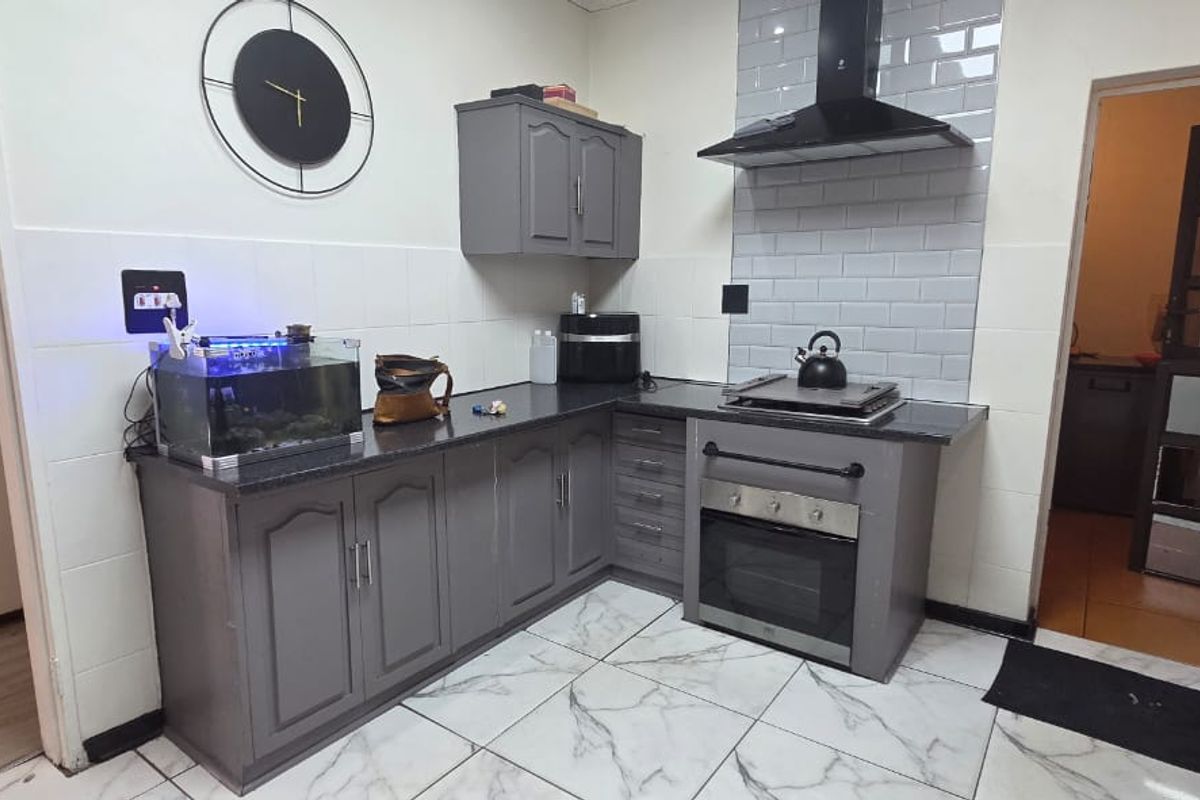 Modern kitchen featuring grey built-in cabinetry, granite countertops, subway tile backsplash, and integrated oven with extractor fan.