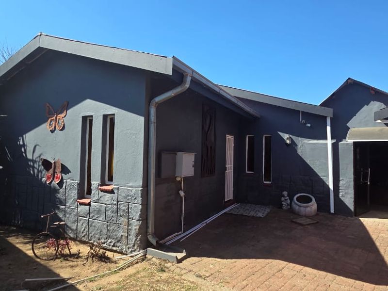 Rear exterior view of the house featuring dark painted walls with stone cladding accents, brick paved courtyard, and functional guttering systems.