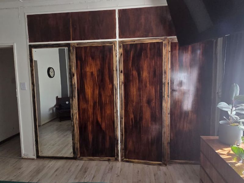 Bedroom featuring built-in wooden cupboards with a mirrored panel and light-toned laminate flooring.