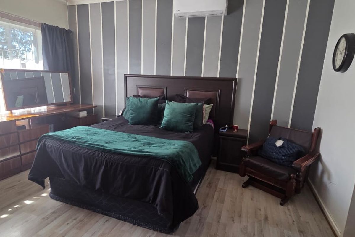 A bedroom featuring laminate flooring, a wall-mounted split-system air conditioner, and a window with security bars.