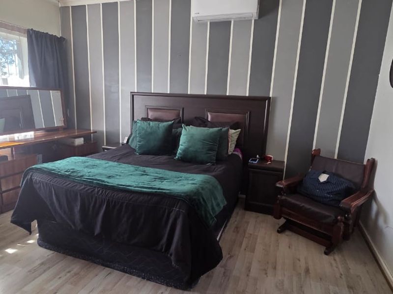 A bedroom featuring laminate flooring, a wall-mounted split-system air conditioner, and a window with security bars.