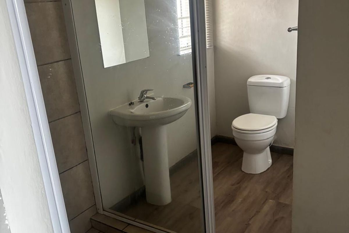 A functional bathroom featuring a pedestal basin, toilet, and a separate shower enclosure with tiled flooring and laminate finishes.