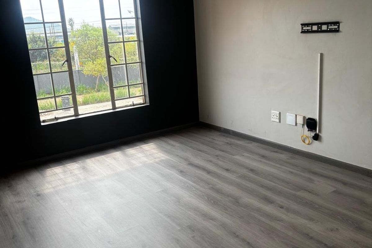 An empty living room featuring modern grey laminate flooring, a large grid window, and wall-mounted TV infrastructure.