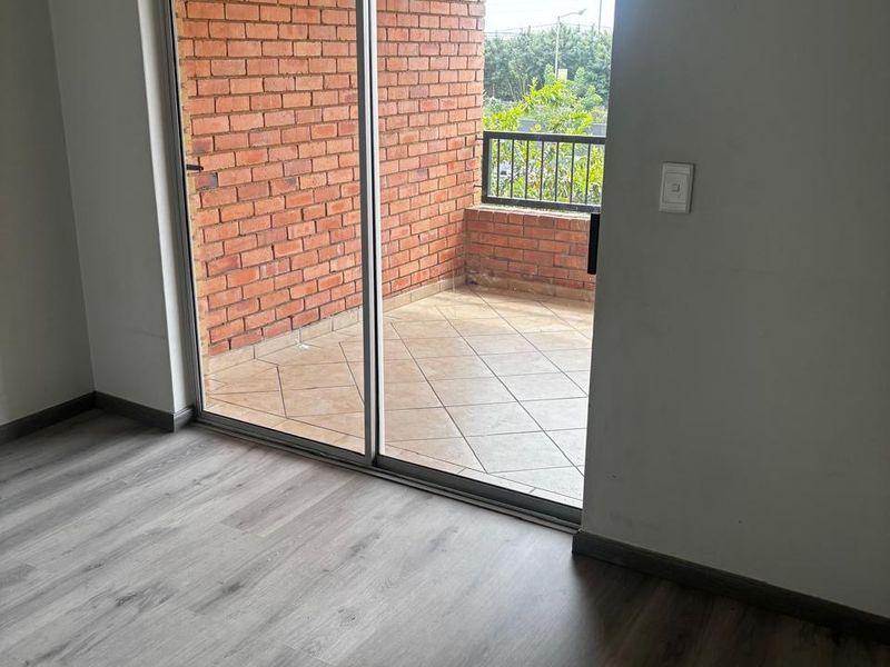 An empty room featuring modern laminate flooring with a sliding glass door leading to a private balcony with exposed brick walls and tiled flooring.