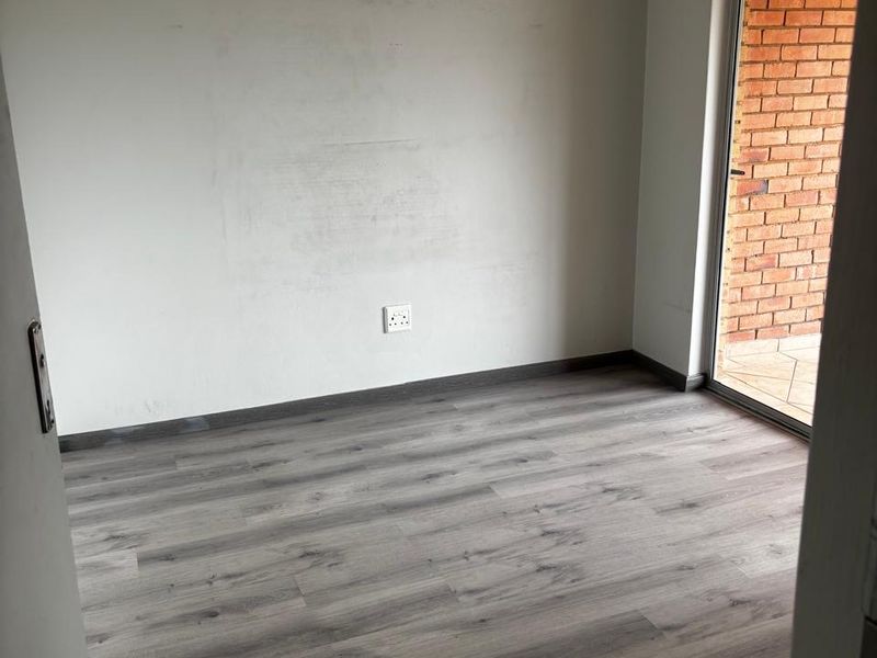 An empty bedroom featuring modern grey laminate flooring, neutral walls, and a sliding glass door providing access to an outdoor area.