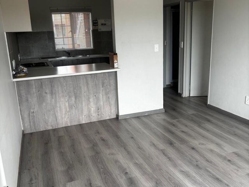 An open-plan living and kitchen area featuring modern grey laminate flooring, a breakfast bar, and neutral wall finishes.