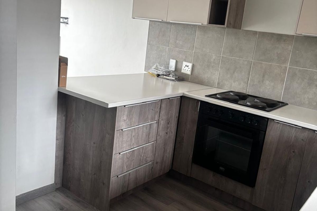 Modern kitchen featuring wood-look cabinetry, laminate countertops, a built-in electric oven and hob, and neutral tiled backsplash.