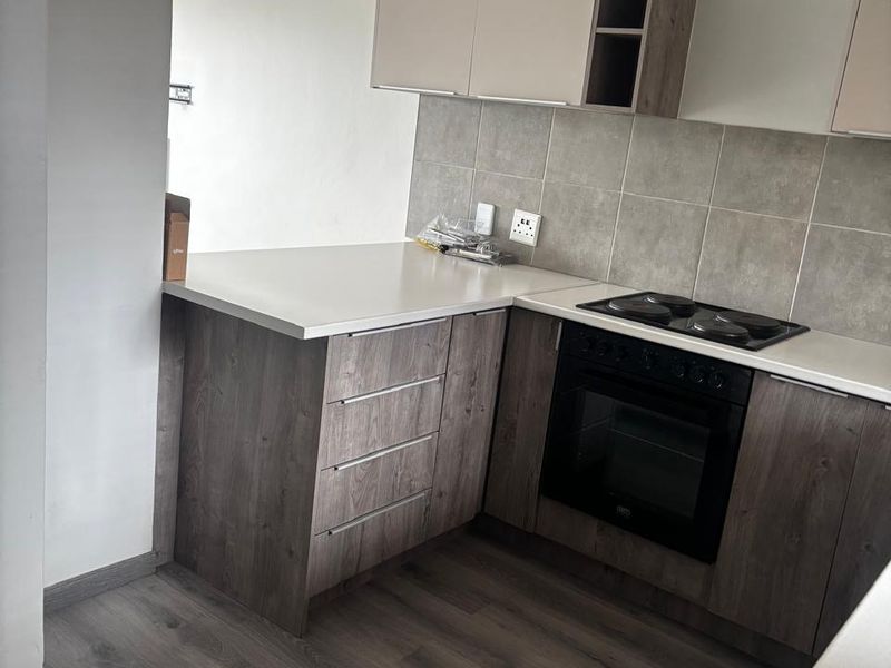 Modern kitchen featuring wood-look cabinetry, laminate countertops, a built-in electric oven and hob, and neutral tiled backsplash.