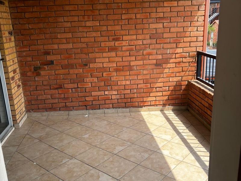 A covered balcony featuring exposed brick walls, tiled flooring, and a metal railing, providing a functional outdoor space.