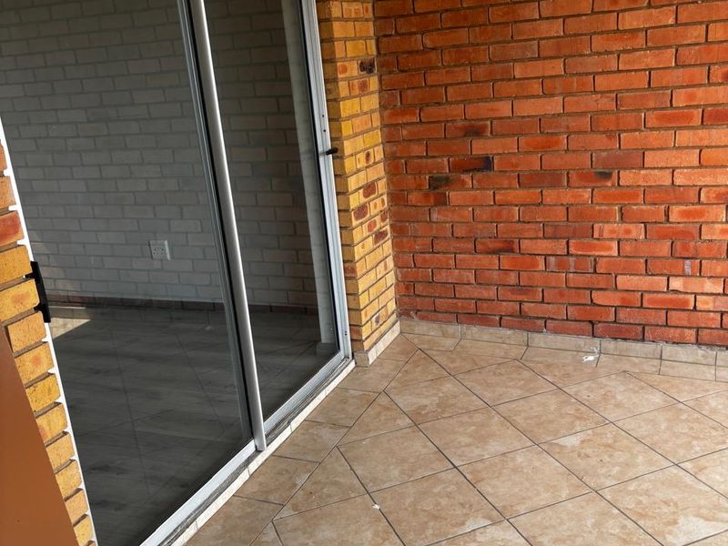 A covered patio area featuring exposed brick walls, tiled flooring, and a sliding glass door providing access to the interior living space.