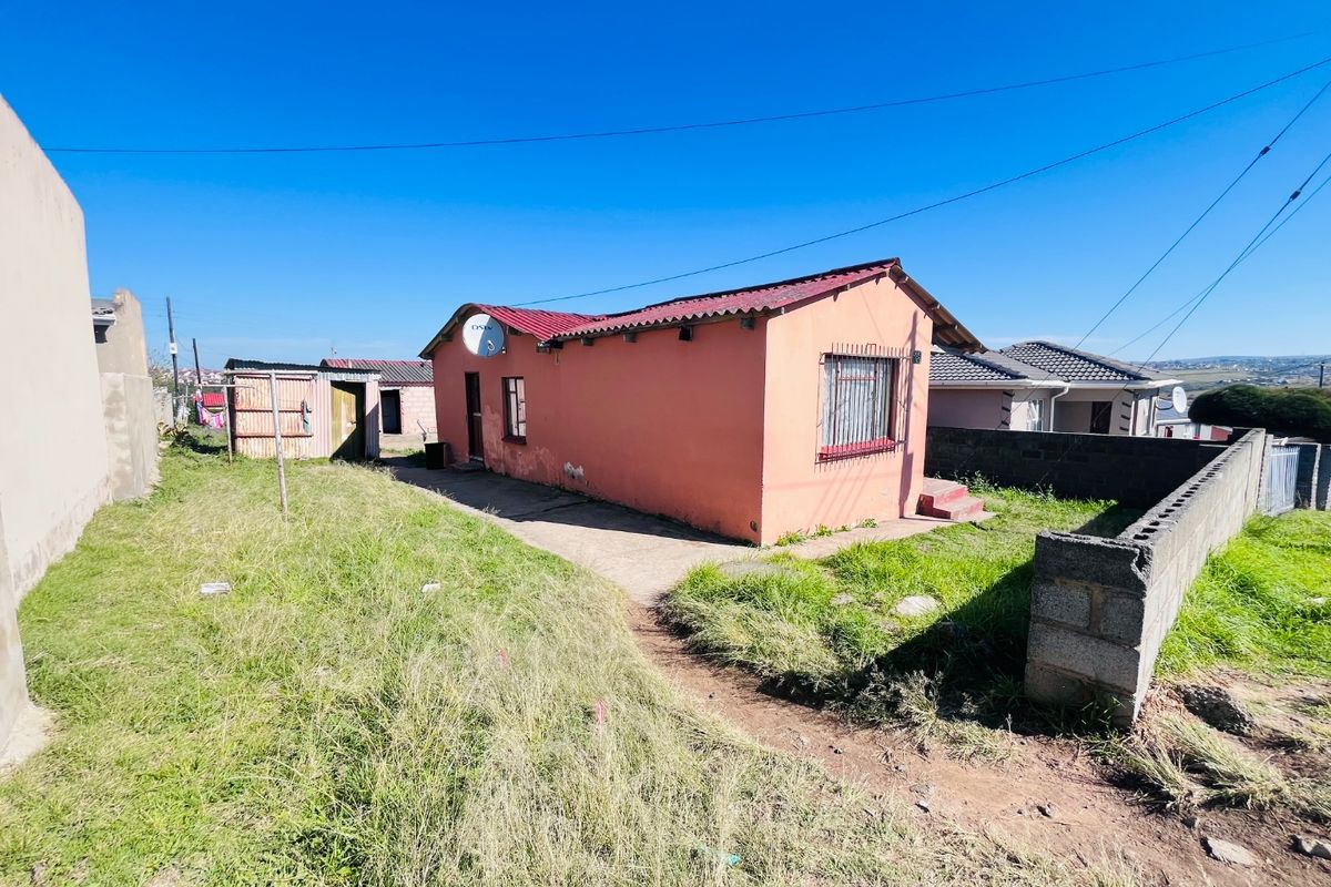 Rear view of a detached house featuring a corrugated metal roof, security bars on windows, and a concrete block boundary wall.