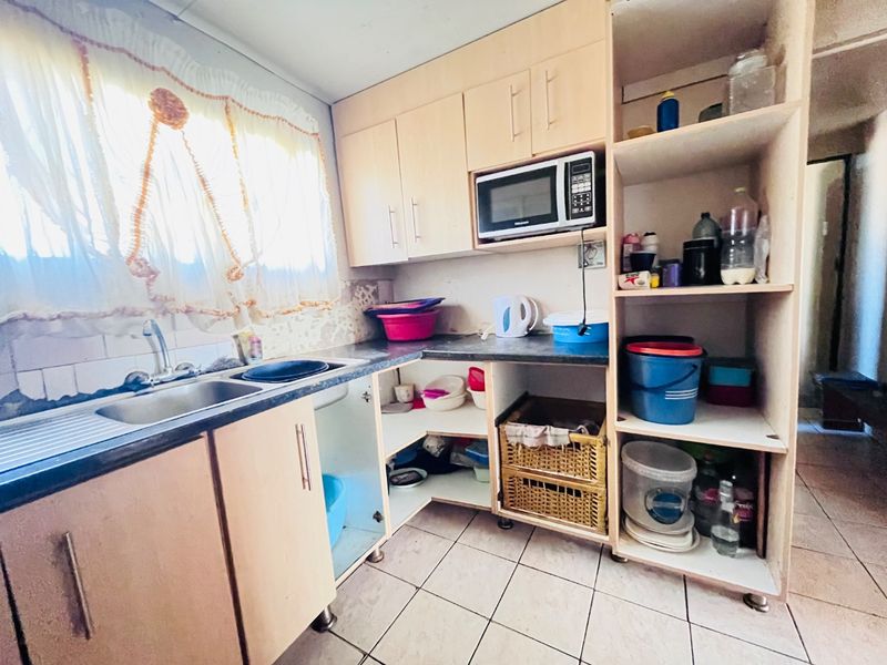 A functional kitchen featuring laminate cabinetry, a built-in microwave, stainless steel sink, and tiled flooring, currently showing signs of wear and missing cabinet doors.
