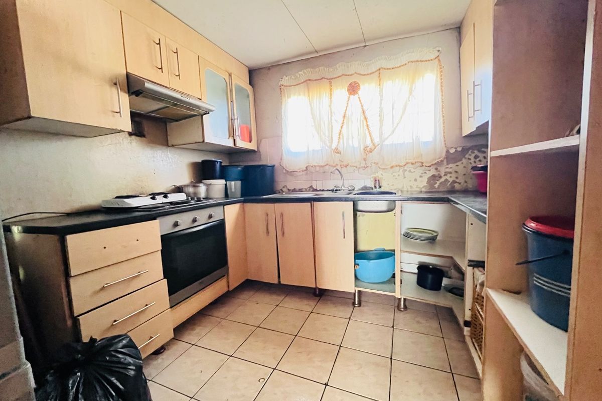A dated kitchen featuring built-in cabinetry, an oven, hob, and extractor fan, requiring cosmetic updates and repairs to wall finishes and cabinetry.