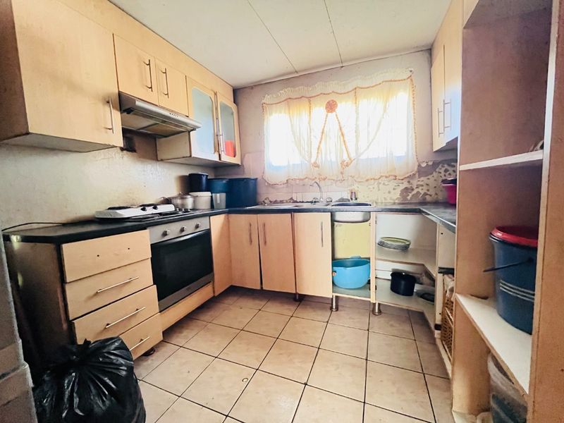 A dated kitchen featuring built-in cabinetry, an oven, hob, and extractor fan, requiring cosmetic updates and repairs to wall finishes and cabinetry.