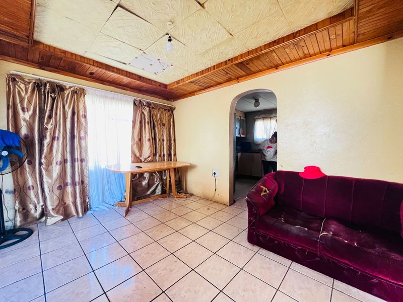 Living room featuring tiled flooring, decorative ceiling tiles with timber trim, and an arched doorway leading to an adjacent room.